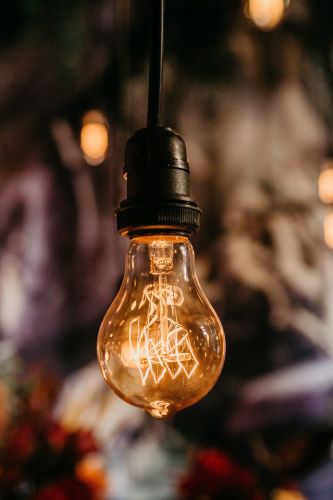 Blown tubular light bulb - on - hanging from a black wire. Photo by Jonathan Borba on Unsplash.